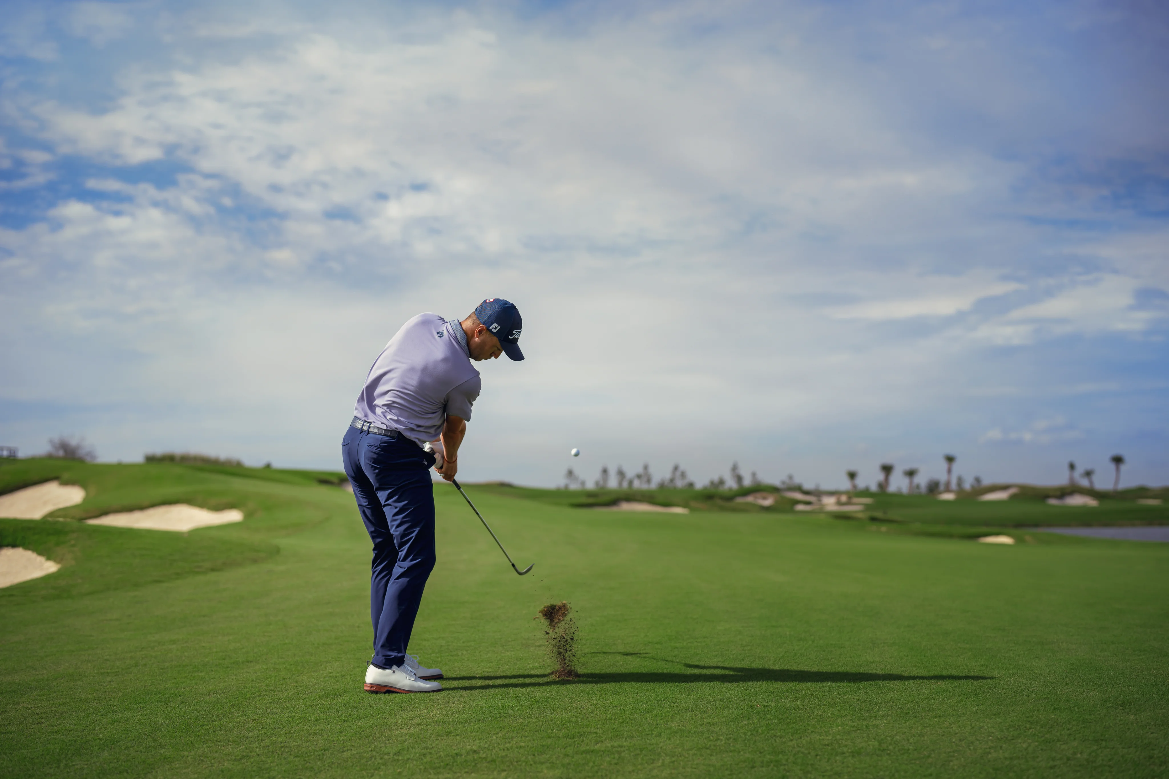 View from behind as a golfer strikes the ball with a swing on the course.