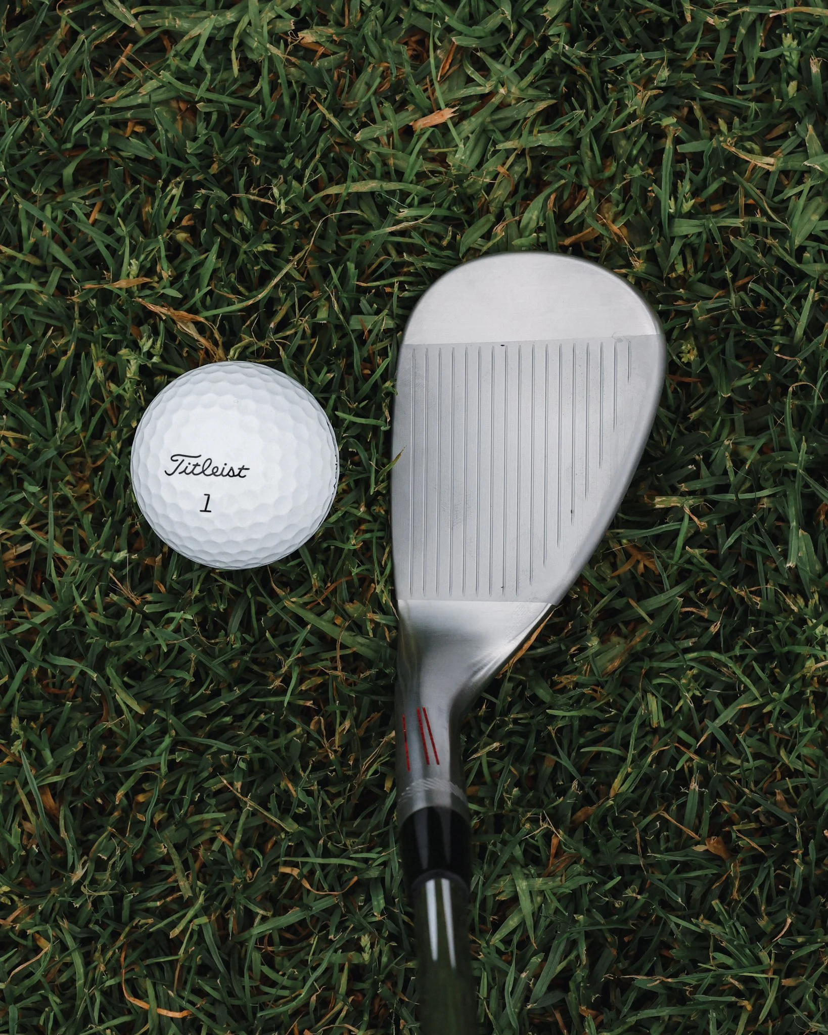 A golf club iron with visible flight lines, placed next to a Titleist golf ball.